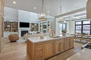 Kitchen with light wood finish cabinetry, an island with sink, decorative light fixtures, light stone counters, and light wood-style floors
