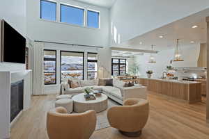 Living room with light wood-type flooring, a glass covered fireplace, recessed lighting, and a high ceiling