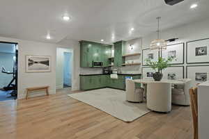 Kitchen with green cabinets, dark countertops, light wood-type flooring, and tasteful backsplash