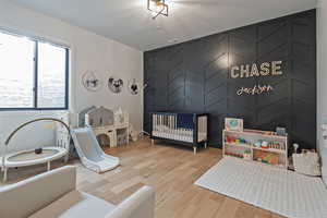 Bedroom with an accent wall, a crib, light wood-type flooring, and a decorative wall