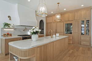 Kitchen featuring arched walkways, light wood-style floors, a center island with sink, gas range, and wine cooler