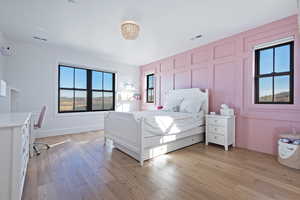 Bedroom with a decorative wall, light wood-style floors, and multiple windows