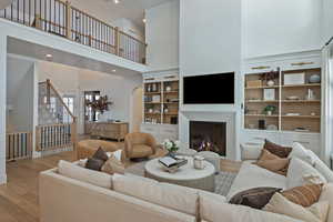 Living area featuring a high ceiling, a warm lit fireplace, wood finished floors, arched walkways, and recessed lighting