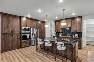 Kitchen with a kitchen bar, stainless steel appliances, decorative light fixtures, a center island with sink, and dark stone counters