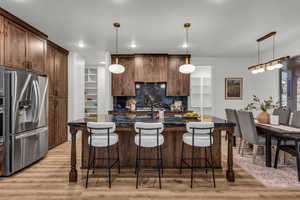 Kitchen with a kitchen bar, a center island with sink, stainless steel refrigerator with ice dispenser, and light wood-style flooring