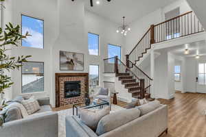 Living area featuring a high ceiling, light wood-type flooring, a brick fireplace, a chandelier, and healthy amount of natural light