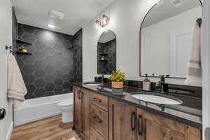 Full bathroom with double vanity, shower / washtub combination, and light wood-style floors