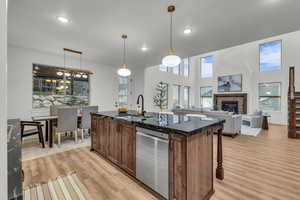 Kitchen with an island with sink, a fireplace, dishwasher, decorative light fixtures, and a high ceiling
