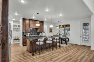 Kitchen with a kitchen breakfast bar, a center island with sink, dark stone countertops, decorative light fixtures, and decorative backsplash