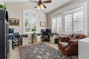 Home office featuring ceiling fan, vaulted ceiling, and light wood-style flooring
