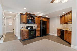 Kitchen with black appliances, decorative backsplash, light stone countertops, dark tile patterned flooring, and recessed lighting