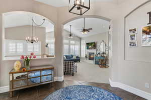 Tiled entrance foyer with suspended lighting, carpet floors, ceiling fan, a glass covered fireplace, and vaulted ceiling