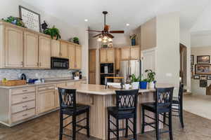 Kitchen with light wood finish cabinetry, a kitchen breakfast bar, ceiling fan, decorative backsplash, and black appliances