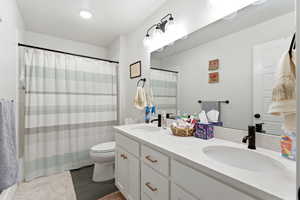 Full bathroom with double vanity, shower / bath combination with curtain, and dark tile patterned flooring