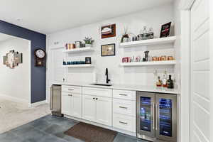 Indoor wet bar with white cabinetry, beverage cooler, light stone counters, dark tile patterned flooring, and dark colored carpet