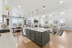 Kitchen featuring open floor plan, a center island with sink, light wood-type flooring, pendant lighting, and dual tone cabinets