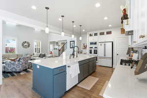 Dual tone kitchen with two tone cabinets, open floor plan, white appliances, glass insert cabinets, and a center island with sink