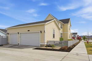 View of side of property with a fenced front yard, driveway, a garage, and a shingled roof
