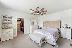 Bedroom with a spacious closet, a ceiling fan, and light colored carpet