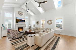 Living room featuring light wood-type flooring, a warm lit fireplace, ceiling fan, and a skylight