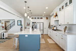 Kitchen featuring hanging light fixtures, light wood finished floors, two tone cabinets, light stone countertops, and a center island with sink