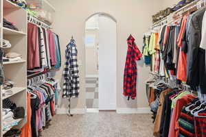 Walk in closet with arched walkways and light colored carpet