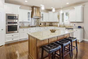Dual tone kitchen with stainless steel appliances, glass insert cabinets, a kitchen island, light granite counters, and a breakfast bar
