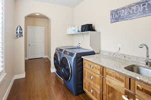 Laundry room with arched walkways, dark wood-type flooring, washer and dryer, sink and cabinet space