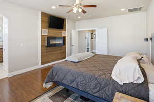 Bedroom with wood finished floors, a ceiling fan, ensuite bathroom, a fireplace, and wooden walls