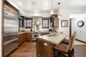 Kitchen with a peninsula, high end appliances, pendant lighting, light stone counters, and dark wood-type flooring