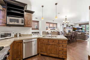 Kitchen with a peninsula, open floor plan, stainless steel appliances, a stone fireplace, and dark wood-style flooring