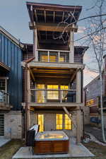Rear view of house with a balcony, a hot tub, and stone siding