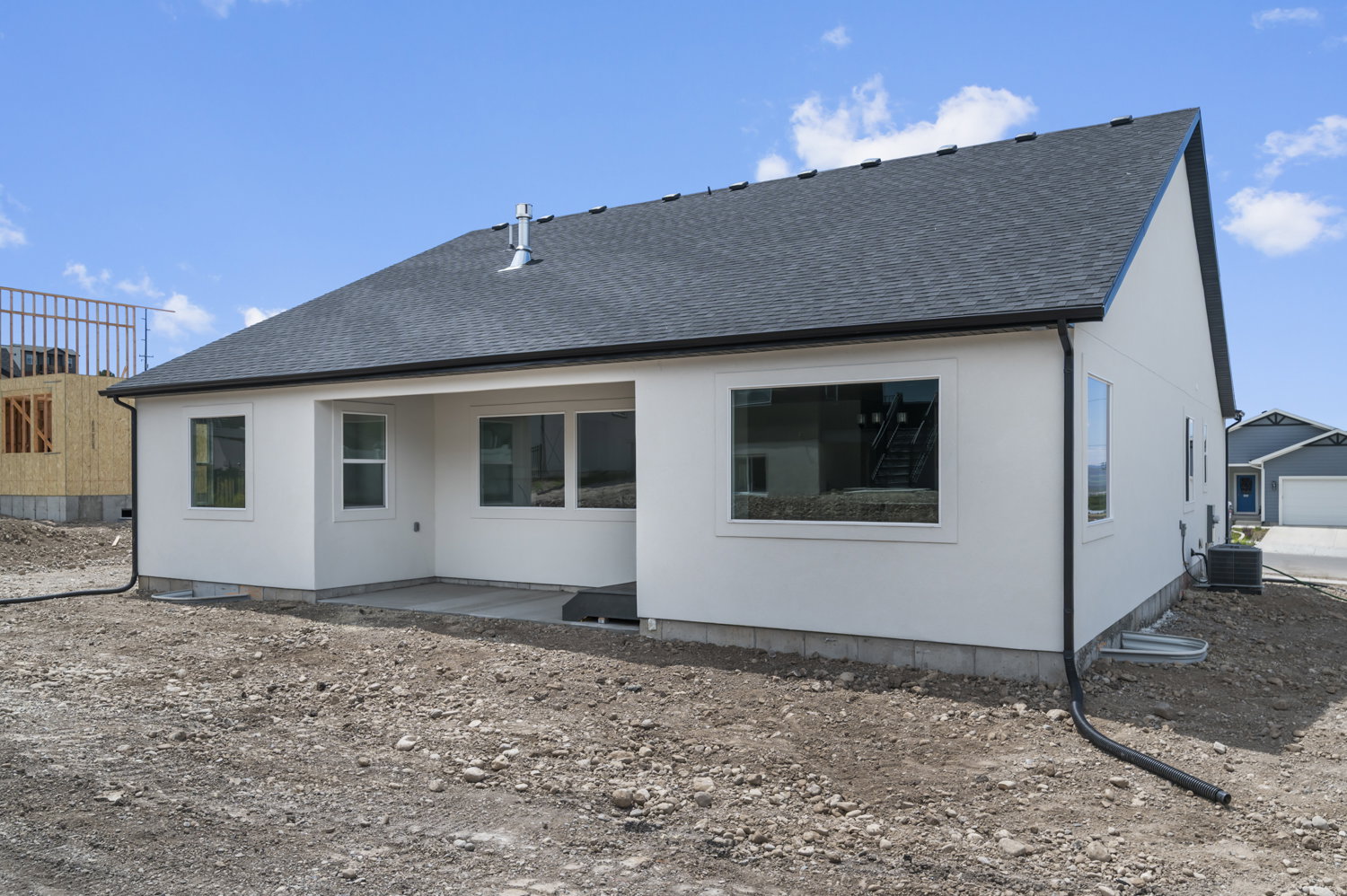 Modern stucco exterior featuring a dark asphalt shingle roof, black gutters, and a concrete patio
