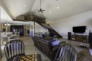 Living room with a high ceiling, light wood-style flooring, a ceiling fan, and suspended lighting
