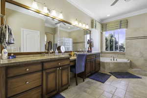 Full bath featuring a ceiling fan, vanity, stone tile flooring, a garden tub, and ornamental molding