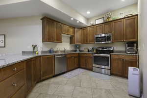 Kitchen featuring stainless steel appliances, wood finish cabinets, light stone counters, and recessed lighting