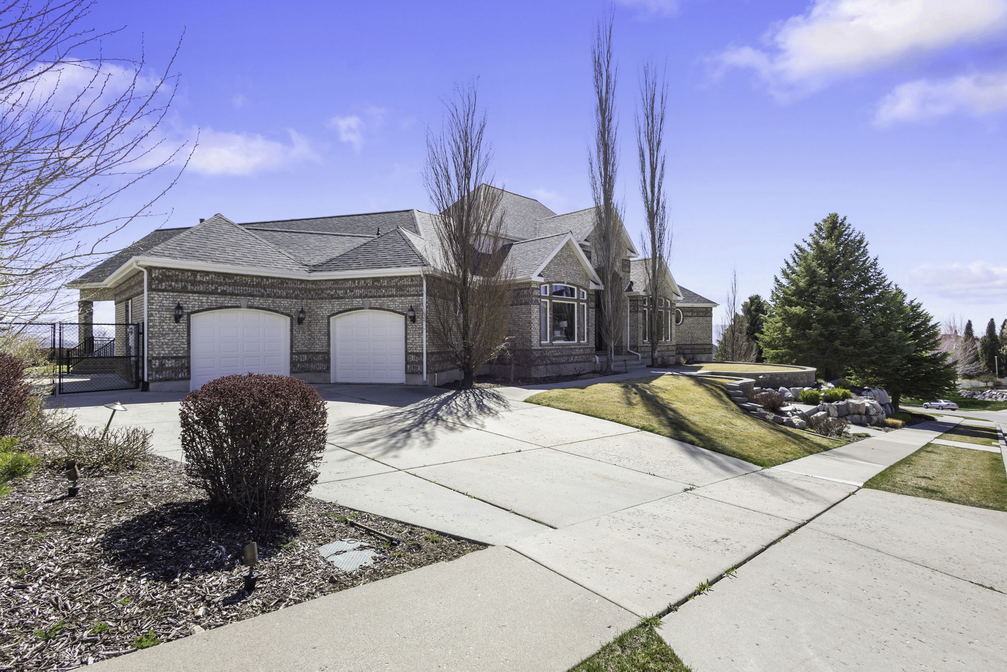 View of front of house with concrete driveway, a garage, a shingled roof, brick siding, and a gate