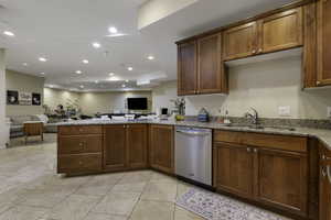 Kitchen featuring a peninsula, open floor plan, light stone countertops, stainless steel dishwasher, and wood finish cabinets