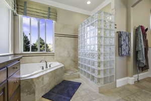 Bathroom featuring a walk in shower, crown molding, a bath, vanity, and stone tile floors