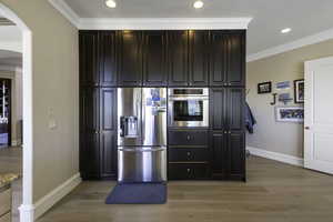 Kitchen featuring crown molding, stainless steel appliances, dark wood finish cabinets, light wood-style floors, and arched walkways
