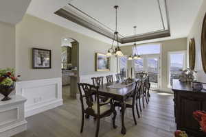 Dining space with a raised ceiling, a mountain view, suspended lighting, arched walkways, and light wood-type flooring