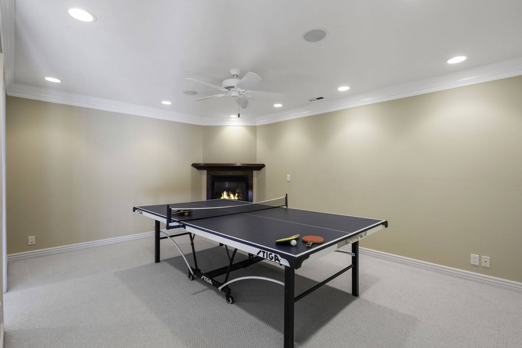 Playroom featuring a glass covered fireplace, light carpet, recessed lighting, a ceiling fan, and ornamental molding