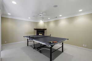 Playroom featuring a glass covered fireplace, light carpet, recessed lighting, a ceiling fan, and ornamental molding