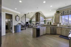 Kitchen featuring a peninsula, ceiling fan, vaulted ceiling, ornamental molding, and light stone countertops