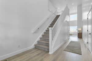 Stairs with a high ceiling, hardwood / wood-style floors, and recessed lighting