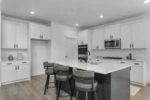 Two tone kitchen with light wood-style floors, stainless steel appliances, a kitchen bar, recessed lighting, and light stone counters
