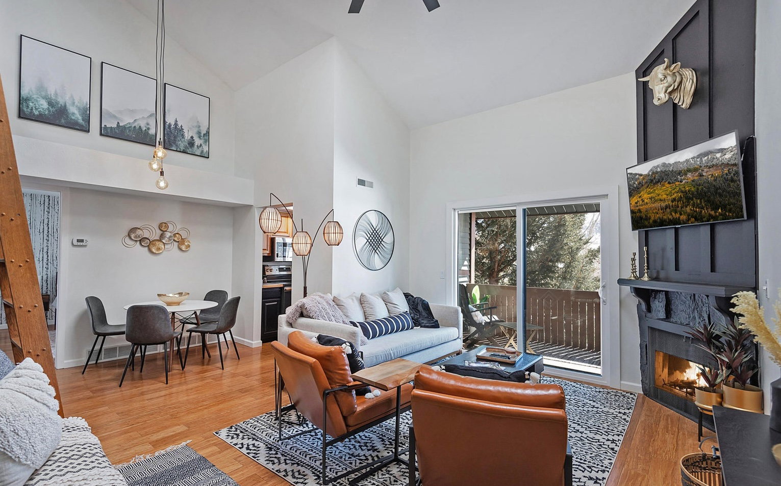 Living area featuring light wood-type flooring, lofted ceiling, a glass covered fireplace, and a ceiling fan