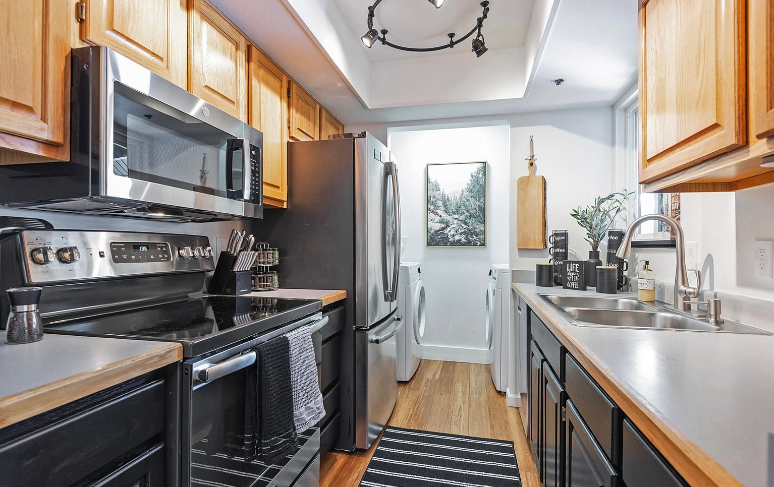 Kitchen with stainless steel appliances, light wood-type flooring, light countertops, dark cabinets, and a raised ceiling