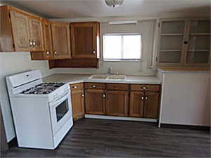 Kitchen featuring white range with gas stovetop, light countertops, wood finish cabinetry, and dark wood-type flooring