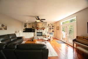 Living area with a textured ceiling, ceiling fan, a stone fireplace, tongue and groove hardwood oak finished floors, and built in shelves